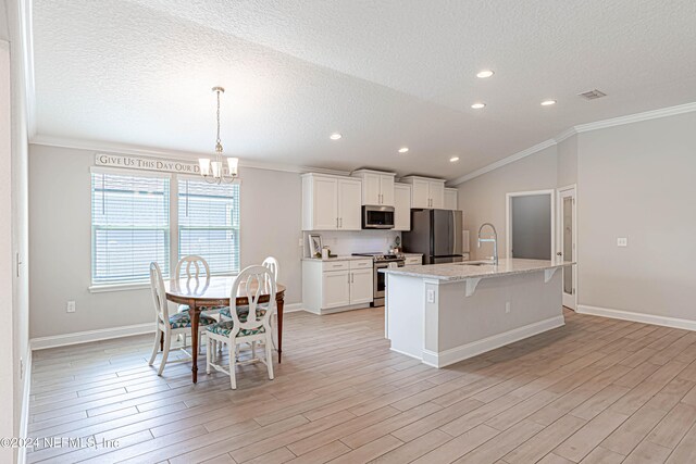 kitchen featuring appliances with stainless steel finishes, light hardwood / wood-style floors, crown molding, an island with sink, and white cabinets