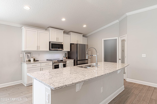 kitchen with appliances with stainless steel finishes, sink, white cabinetry, crown molding, and an island with sink