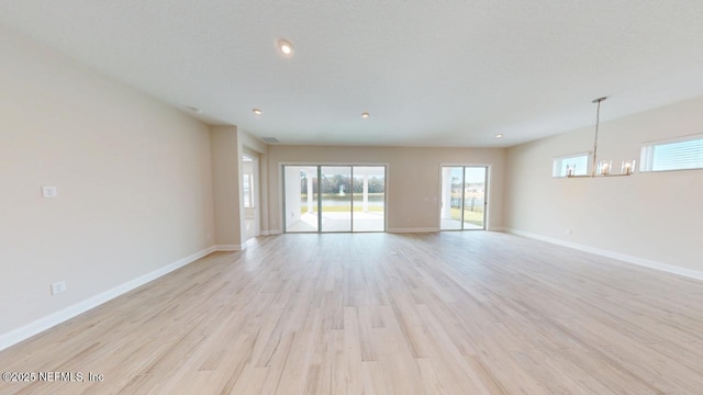 spare room featuring an inviting chandelier, light wood-style flooring, and baseboards