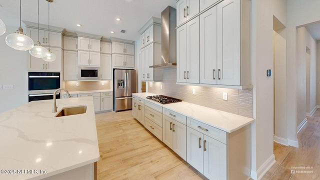 kitchen featuring wall chimney exhaust hood, a sink, stainless steel appliances, light wood-style floors, and backsplash