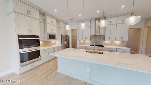 kitchen featuring light stone counters, tasteful backsplash, light wood-style flooring, appliances with stainless steel finishes, and wall chimney exhaust hood