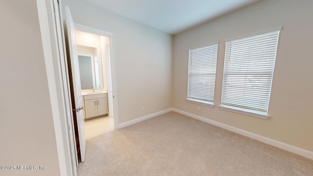 unfurnished room featuring baseboards, a sink, and light colored carpet