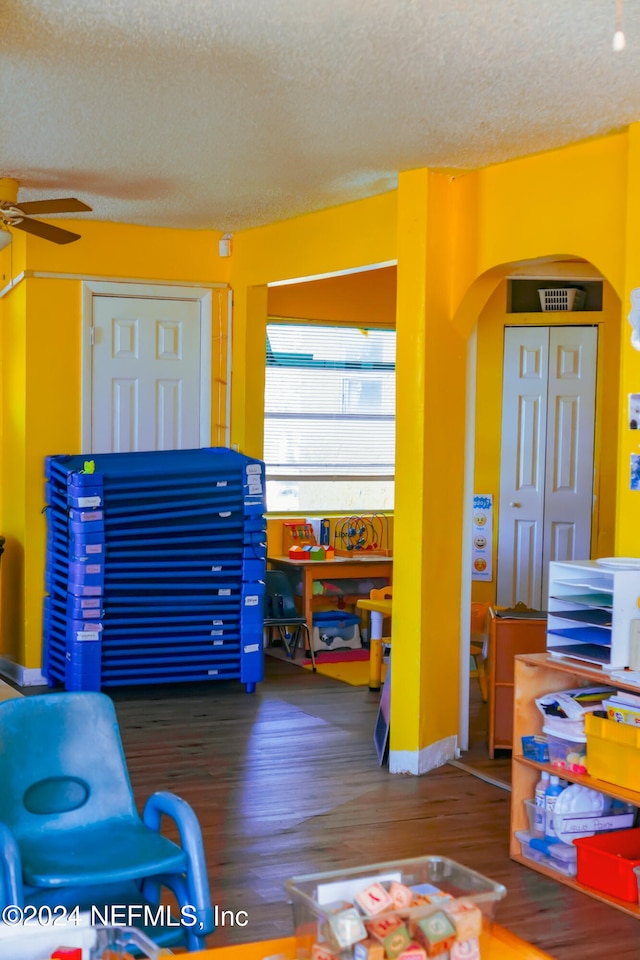 playroom featuring a textured ceiling, dark hardwood / wood-style flooring, and ceiling fan