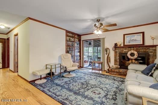 living room featuring crown molding, wood-type flooring, a brick fireplace, and ceiling fan