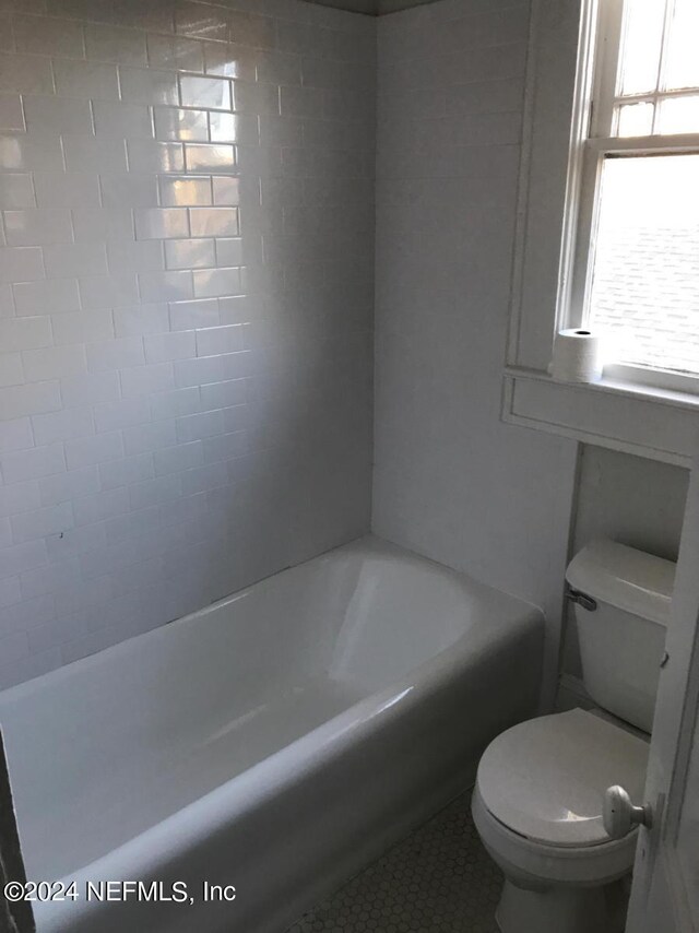 bathroom with tile flooring, tiled shower / bath combo, and toilet