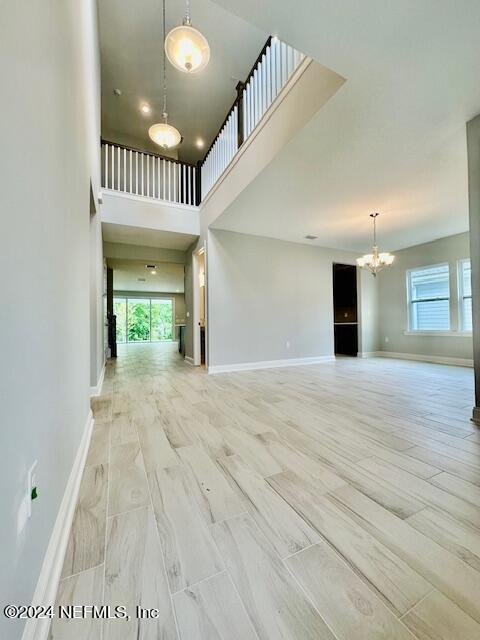 unfurnished living room with a wealth of natural light, a notable chandelier, a high ceiling, and baseboards