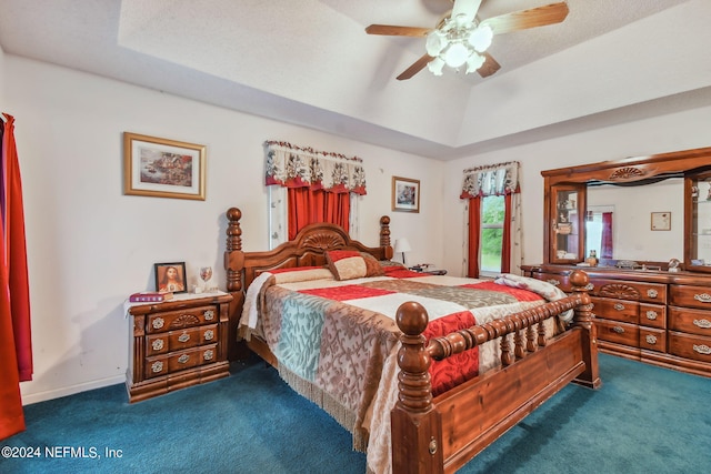 bedroom with ceiling fan, a raised ceiling, dark carpet, and a textured ceiling