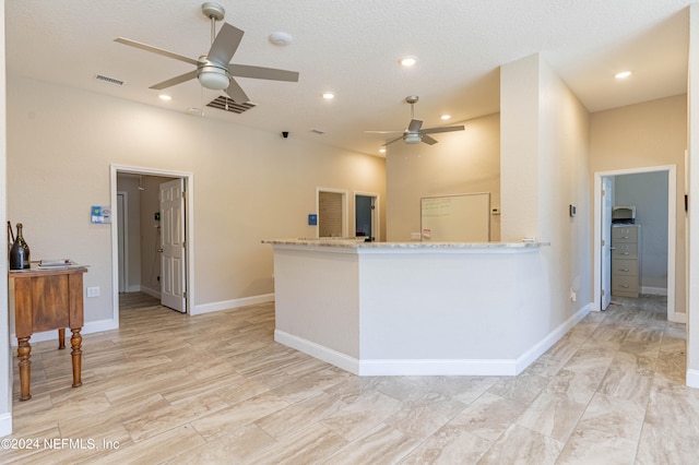 kitchen with kitchen peninsula, ceiling fan, and light stone counters