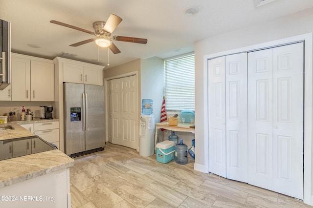 kitchen with ceiling fan, light stone counters, stainless steel refrigerator with ice dispenser, and white cabinetry