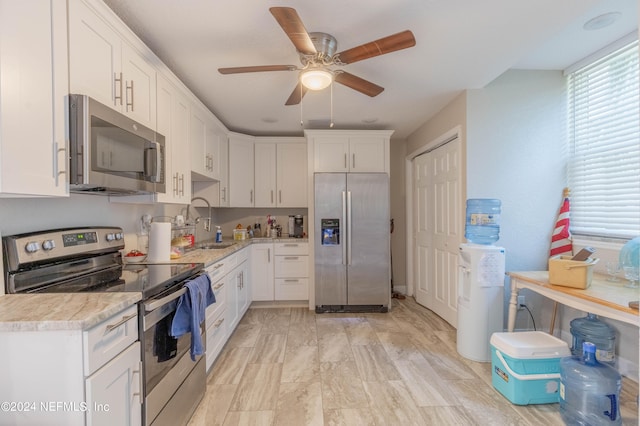 kitchen featuring appliances with stainless steel finishes, white cabinets, light stone counters, sink, and ceiling fan