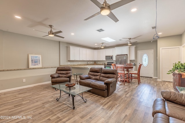 living room with ceiling fan, a skylight, and light hardwood / wood-style flooring