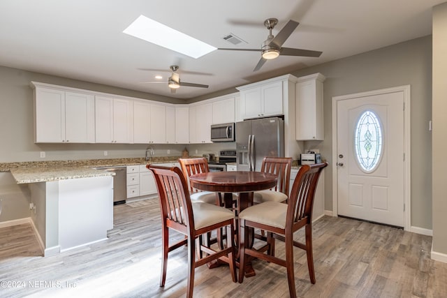 kitchen with white cabinetry, light wood-type flooring, stainless steel appliances, ceiling fan, and a skylight