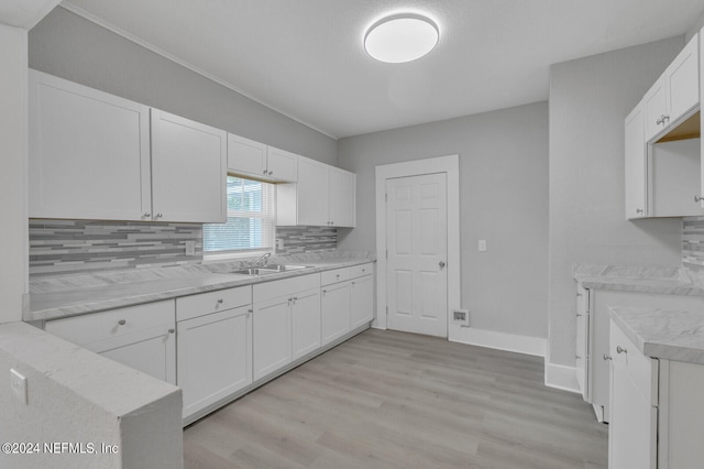 kitchen with light hardwood / wood-style flooring, tasteful backsplash, sink, and white cabinetry