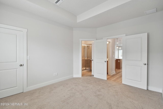 unfurnished bedroom featuring ensuite bathroom and light colored carpet