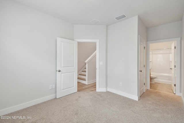 unfurnished bedroom featuring light colored carpet and ensuite bathroom