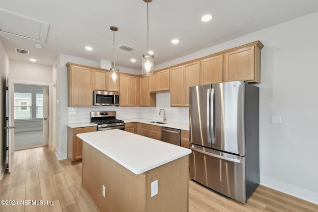 kitchen with sink, stainless steel appliances, light hardwood / wood-style flooring, decorative light fixtures, and a kitchen island