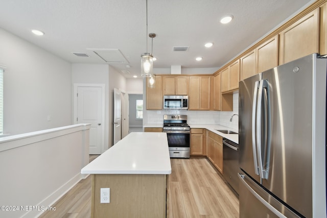 kitchen featuring appliances with stainless steel finishes, sink, light hardwood / wood-style flooring, a center island, and hanging light fixtures