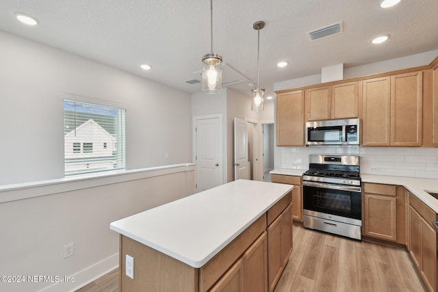 kitchen with appliances with stainless steel finishes, backsplash, pendant lighting, light hardwood / wood-style flooring, and a kitchen island