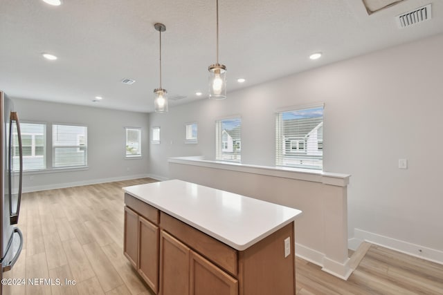 kitchen featuring a center island, a healthy amount of sunlight, decorative light fixtures, and light hardwood / wood-style floors