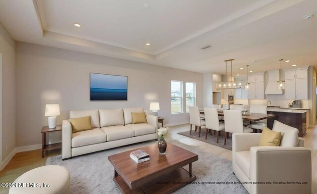 living room with light wood-type flooring, a tray ceiling, sink, and a notable chandelier