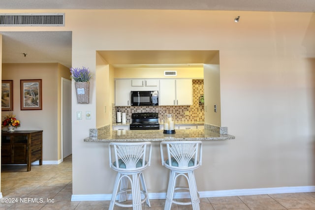 kitchen with white cabinetry, light tile floors, light stone counters, range with electric cooktop, and tasteful backsplash