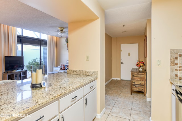 kitchen featuring light stone counters, ceiling fan, light tile floors, a textured ceiling, and white cabinets