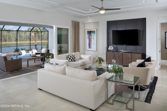 living room featuring ceiling fan, a raised ceiling, and a water view