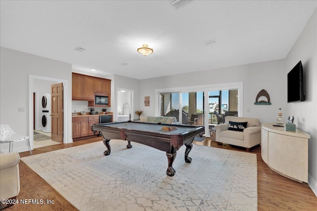 playroom with a textured ceiling, stacked washer and clothes dryer, light hardwood / wood-style floors, and billiards