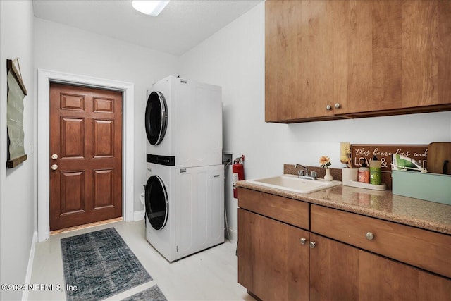 laundry room with stacked washer and dryer, sink, and cabinets