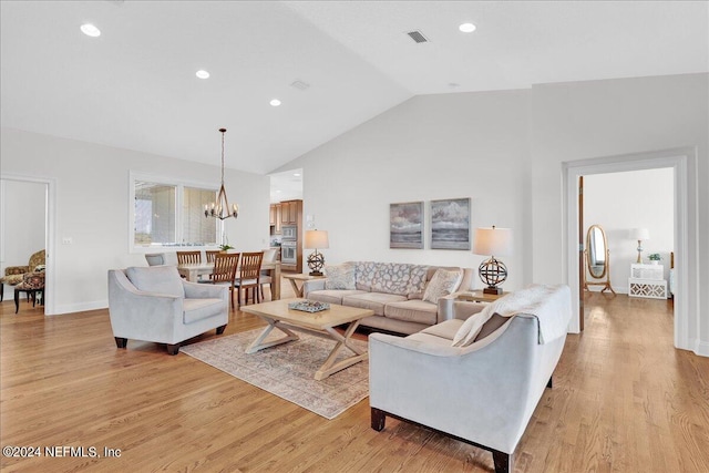 living room with vaulted ceiling, an inviting chandelier, and light hardwood / wood-style floors