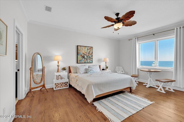 bedroom featuring ceiling fan, crown molding, a water view, and hardwood / wood-style floors