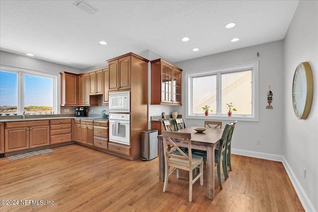 kitchen with decorative backsplash, a wealth of natural light, white appliances, and light hardwood / wood-style flooring