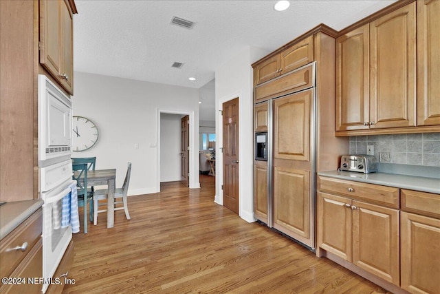 kitchen featuring backsplash, light hardwood / wood-style flooring, a textured ceiling, and built in appliances