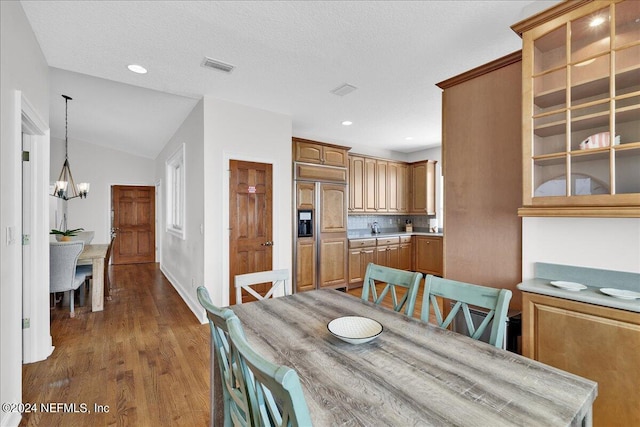 dining room with vaulted ceiling, a textured ceiling, a chandelier, and hardwood / wood-style flooring