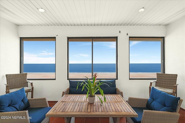 sunroom with a healthy amount of sunlight, a water view, and a beach view