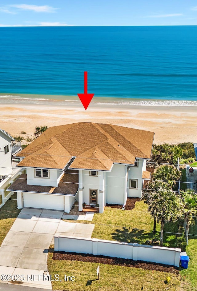 view of front facade featuring a water view, a front lawn, a view of the beach, and a garage