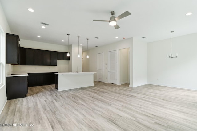 kitchen with ceiling fan with notable chandelier, light hardwood / wood-style floors, a kitchen island with sink, and hanging light fixtures