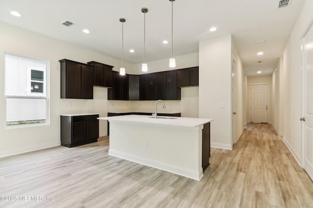 kitchen featuring light hardwood / wood-style flooring, an island with sink, hanging light fixtures, and sink