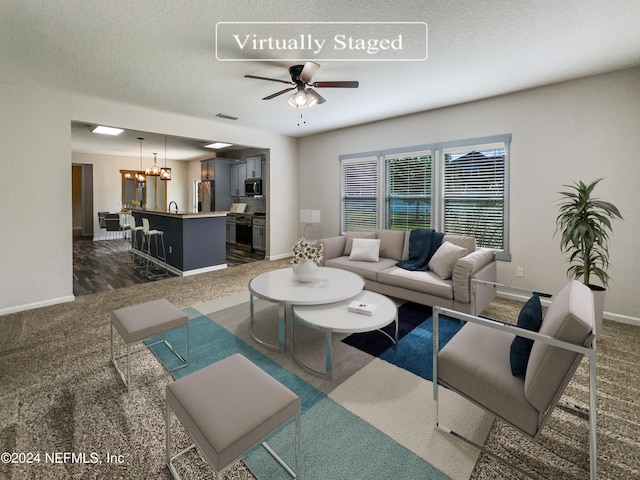 carpeted living room featuring ceiling fan with notable chandelier, a textured ceiling, and sink