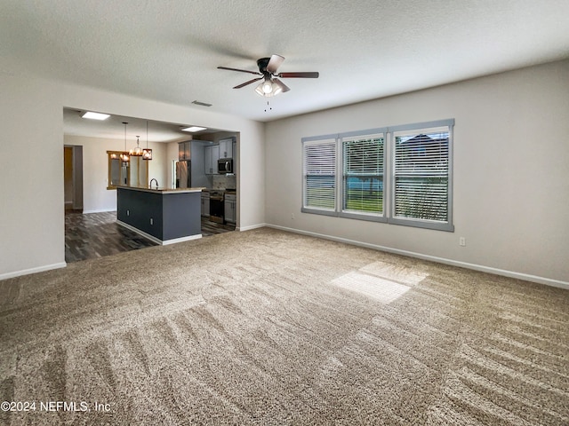 unfurnished living room with ceiling fan with notable chandelier, dark colored carpet, sink, and a textured ceiling