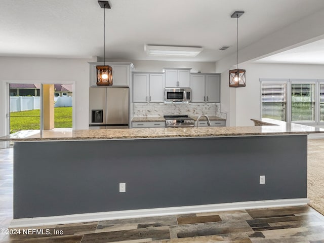 kitchen featuring appliances with stainless steel finishes, tasteful backsplash, an island with sink, and hanging light fixtures