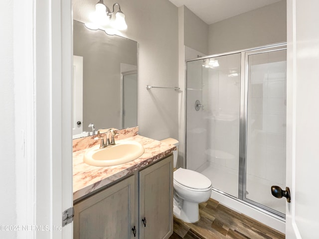 bathroom featuring hardwood / wood-style floors, vanity with extensive cabinet space, an enclosed shower, and toilet