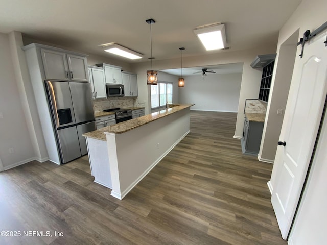 kitchen with pendant lighting, gray cabinets, stainless steel appliances, light stone counters, and a barn door