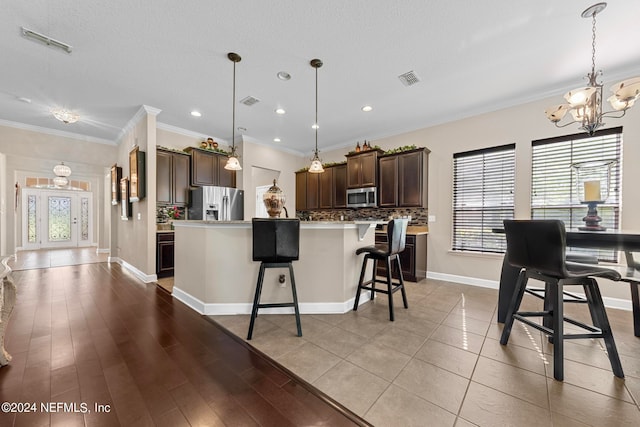 kitchen with a center island with sink, light wood-type flooring, pendant lighting, backsplash, and appliances with stainless steel finishes