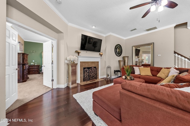 carpeted living room with ceiling fan, a tile fireplace, a textured ceiling, and crown molding