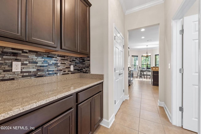 kitchen featuring light stone counters, light tile flooring, backsplash, ornamental molding, and dark brown cabinets