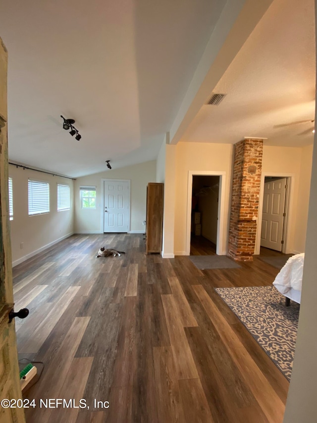 unfurnished living room with dark hardwood / wood-style floors, vaulted ceiling, and brick wall