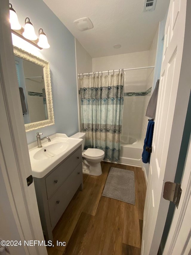 full bathroom featuring wood-type flooring, vanity with extensive cabinet space, shower / bath combination with curtain, and toilet