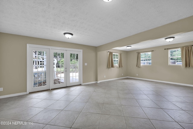 tiled empty room with a textured ceiling, a wealth of natural light, and french doors