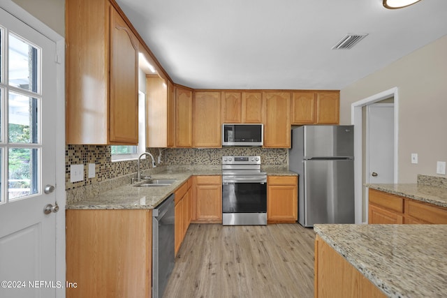 kitchen with appliances with stainless steel finishes, sink, light stone counters, and light hardwood / wood-style floors